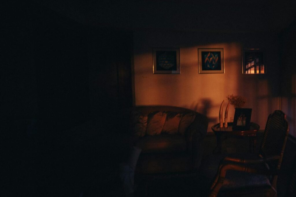 Ugaona fotelja osvetljena toplim svetlom pored stočića sa vazom i ramom za slike